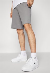 Bermudas de algodón grises con un ajuste relajado, que presentan un pequeño logo en el muslo, combinadas con zapatillas blancas y calcetines de canalé.