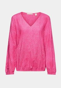 Blouse rose à manches longues avec des pois blancs, col en V, poignets et ourlet élastiques, présentée sur un fond uni.