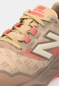 Beige sneakers med en mesh-overdel, grå og neon akcenter, teksturerede mønstre og en polstret tunge med branding. Snørebånd i blødt beige.