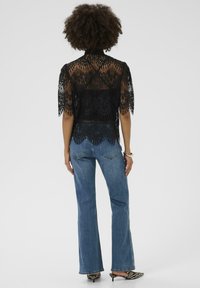 Zwart kanten top met korte mouwen, hoge halslijn, schulpzoom, gecombineerd met blauwe flare jeans en stijlvolle zwart-witte patternd schoenen.