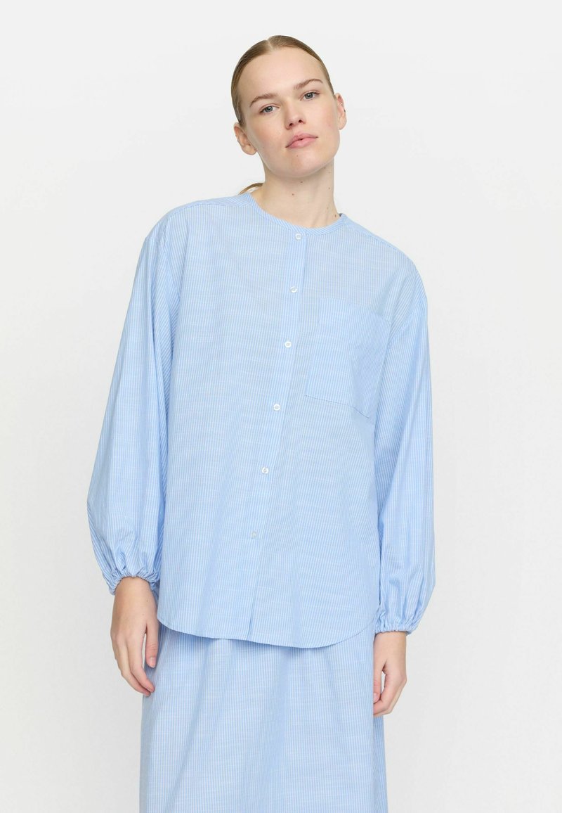 Camicia blu a righe con colletto arrotondato, maniche lunghe a sbuffo e tasca sul petto. Tessuto morbido con una texture leggera.