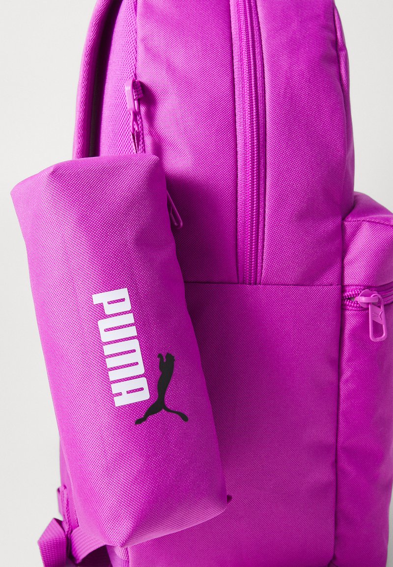 Sac à dos en tissu violet avec une poche zippée à l'avant. Présente un grand logo "PUMA" en blanc et une silhouette noire d'un puma. Fini texturé.