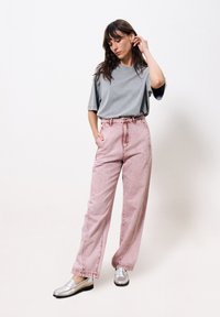 Hellgraues, übergroßes T-Shirt mit kurzen Ärmeln, kombiniert mit hoch taillierten, rosa Jeanshosen in lockerer Passform und sichtbaren Nähten. Silberne Loafers.