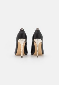 Chaussures à talons hauts en cuir noir avec un talon métallique doré brillant et des accents texturés à la base. Design minimaliste avec un bout pointu.