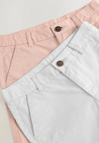 Lichtroze en lichtgrijze chino's met knoopsluitingen, voorzien van een vlakke voorkant, zijzakken en gladde katoenen stof.