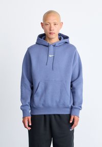 Felpa con cappuccio Nike di colore azzurro chiaro, dotata di una tasca frontale a marsupio, cappuccio con cordini e un piccolo logo giallo sul petto.