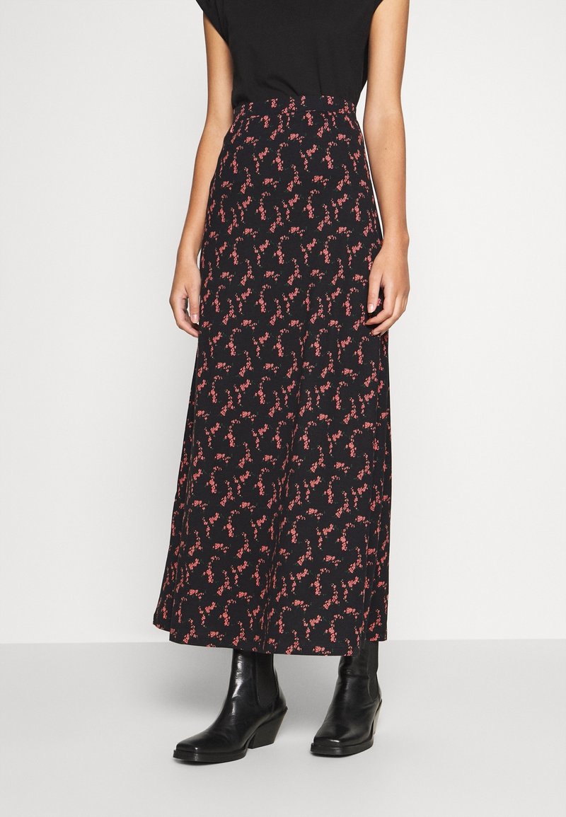 Femme portant une jupe noire longueur cheville avec de petits motifs floraux rouges et des bottines noires.