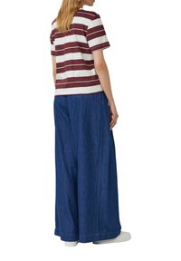 Gestreept katoenen T-shirt in bordeauxrood en wit, gecombineerd met ruime blauwe denim broeken. Witte schoenen maken de outfit compleet.