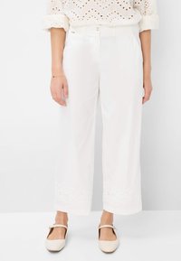 Weiße weit geschnittene Hosen mit einem bestickten Spitzenakzent am Saum, mit einem Knopfverschluss und Seitentaschen. Glatte Textur des Stoffes.