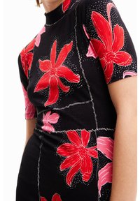 Robe noire à côtes avec manches courtes, ornée de grands motifs floraux rouges et roses, soulignés de coutures blanches, avec des accents en pois.