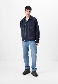 Mornarji modra jakna z belim šivom, zapiranje na gumb in dvema sprednjima žepoma. Oblečena z svetlo modrimi kavbojkami in črnimi športnimi copati.