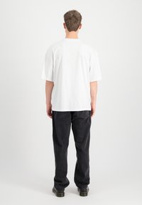 Biely oversized tričko s krátkymi rukávmi, kombinované s voľnými čiernymi džínsami. Minimalistický dizajn, bez viditeľných vzorov alebo akcentov.