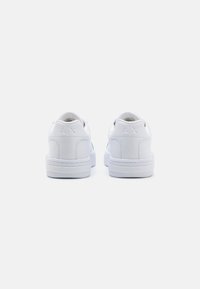 White leather sneakers with smooth texture, rounded shape, padded collar, and rubber sole. "A/X" logo embossed on the heel.