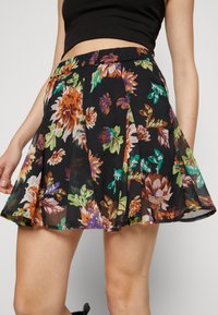 Jupe noire à motif floral avec une ceinture élastique, présentant des fleurs vibrantes orange, vertes et violettes. Coupe évasée, tissu léger.