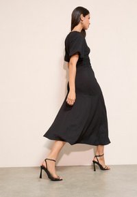 Fekete midi ruha texturált anyagból, rövid, buborék ujjú és alakra szabott derékkal. Fekete, bokapántos, magas sarkú szandálokkal párosítva.