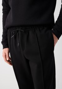 Black sweatpants with a drawstring waist, featuring side pockets and a smooth, slightly textured fabric. The waistband is elasticized.