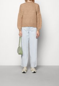 Beżowy prążkowany sweter z wysokim dekoltem, jasnoniebieskie jeansy o prostych nogawkach oraz zielona teksturowana torebka. Buty w kolorze kremowym z akcentami.