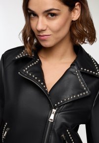 Giacca da motociclista in pelle nera con dettagli in metallo argentato sui colletto e sulle tasche con zip, caratterizzata da un design classico con revers.