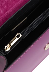 Lila Lederhandtasche Innenraum mit einem schwarzen Reißverschlussfach, goldenen Reißverschlussbeschlägen und glatter Oberfläche mit detaillierter Naht.