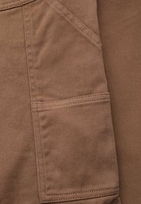 Tela marrón con un bolsillo con una Costura visible y una superficie texturizada. El material parece duradero con un ligero patrón de acanalado.