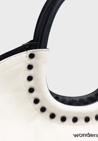 Torba canvas w kremowym kolorze z czarną skórzaną lamówką. Posiada czarne ćwieki wzdłuż zakrzywionego szwu oraz mocny uchwyt dla lepszego chwytu.