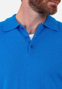 Blaues Poloshirt aus strukturiertem Strickstoff. Mit umgelegtem Kragen, dreiknöpfiger Knopfleiste und einem dezenten Rippmuster.
