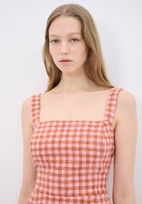 Abito a quadri rosa e arancione con scollatura quadrata e spalline spesse. Presenta un tessuto testurizzato con un motivo a griglia. Senza dettagli visibili.