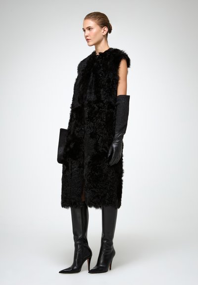 Gilet in pelliccia sintetica nera senza maniche, abbinato a guanti neri e stivali in pelle over-the-knee dal design elegante. Tessuto liscio e punta affusolata.