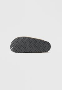 Rubber sole with a textured, black surface featuring a diamond pattern. Rounded front edge with a light-colored accent at the heel.