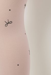 Ljust rosa figurnära tyg med svarta rosett- och prickmönster, slät textur och en strömlinjeformad silhuett. Inga synliga sömmar eller hårdvara.