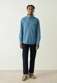 Lichtblauw overhemden met lange mouwen en een borstzak, gecombineerd met donkere spijkerbroeken en beige moccasin-stijl schoenen.