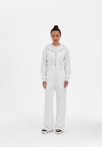 Felpa bianca con zip e design crop, abbinata a pantaloni bianchi a vestibilità morbida. Presenta una texture morbida e sneakers bianche e nere.