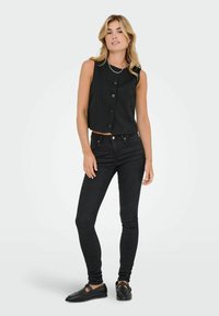 Černý bezrukávový top s proužky a zapínáním na knoflíky, ve spojení s černými slim-fit džíny a černými plochými botami. Hladká struktura a zkrácený design.