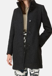 Sort uldblandet frakke med en tekstureret finish, der har en høj krave og fem knaplukninger. Designet inkluderer lange ærmer og en lige pasform.