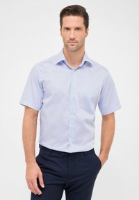 Kurzarmhemd in Hellblau mit geometrischem Muster, Knopfverschluss und klassischem Kragen, kombiniert mit dunklen Hosen.