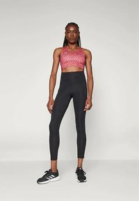 Černé legíny s vysokým pasem v kombinaci s růžovým vzorovaným sportovním podprsenkou. Oblečení je vyrobeno z elastického materiálu a má těsný střih.