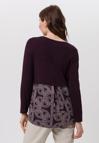 Langsleeve top met een donkerpaarse bovenkant en een gepatternerde onderkant met in elkaar verweven geometrische lijnen in lichte kleuren.