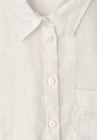 Chemise en lin blanche devant avec col, trois boutons blancs et une poche poitrine sur le côté droit.