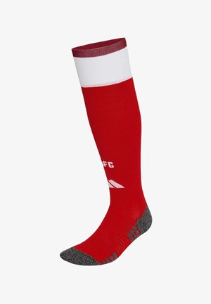 Chaussette de sport rouge montante jusqu'au genou avec bande blanche près du haut, orteil et talon renforcés gris, et texte blanc partiel ainsi que logo sur le mollet.