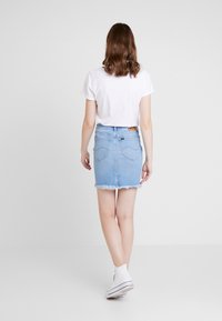 Light blue denim mini skirt with frayed hem, featuring two back pockets and a woven label on the waist. Paired with a white t-shirt and sneakers.
