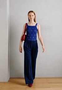 Débardeur en tricot bleu avec encolure carrée, orné de petits accents blancs. Assorti à un pantalon taille haute bleu marine et un sac à main rouge.