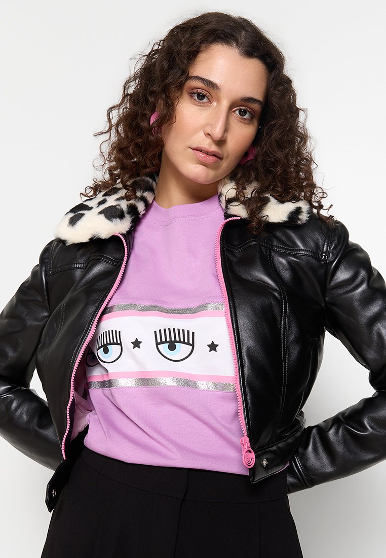 Schwarze Kunstlederjacke mit einem Leopardenmusterkragen, pinkem Reißverschluss, getragen über einem helllila T-Shirt mit Augengrafiken und Glitzerdetails.