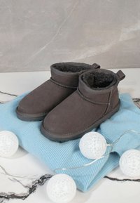 Botas de tobillo de color gris oscuro, hechas de suave ante, con un forro acolchado, costuras en contraste y una suela de goma, colocadas sobre una tela de punto azul.