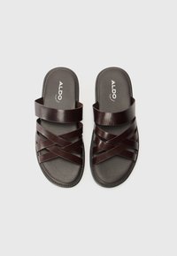Sandales en cuir marron à glissière avec des brides croisées et une semelle plate. Présentent une semelle intérieure texturée et un logo de marque embossé sur le pied.