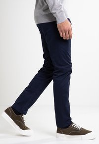 Námořnické modré slim fit kalhoty vyrobené z bavlněné směsi, doplněné tmavě zelenými teniskami s bílou podešví a tkaničkami. Texturovaný, pohodlný design.