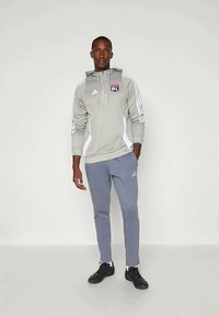 Grey athletic hoodie with a zipper and logo, white accents, paired with light grey tapered pants. Black shoes complete the outfit.