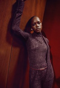 Lace jumpsuit in deep purple with form-fitting design, high collar, and long sleeves. Accented with a thin, jeweled belt.