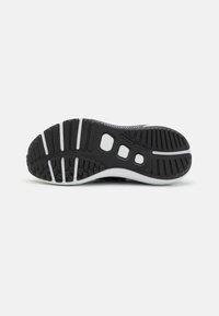 Semelle de chaussure en noir et blanc avec un motif de bande de roulement texturé, des rainures horizontales, des coussinets d'adhérence circulaires et trois découpes rectangulaires dans la zone de la semelle intermédiaire.