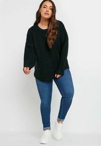 Svart strukturerad stickad tröja med lös passform, kombinerad med blå tajta jeans och vita sneakers. Långa ärmar och rundad nederkant.