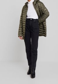 Olivgrön puffjacka med kviltat mönster och huva, i kombination med svarta högmidjade jeans och svarta ank stövlar.